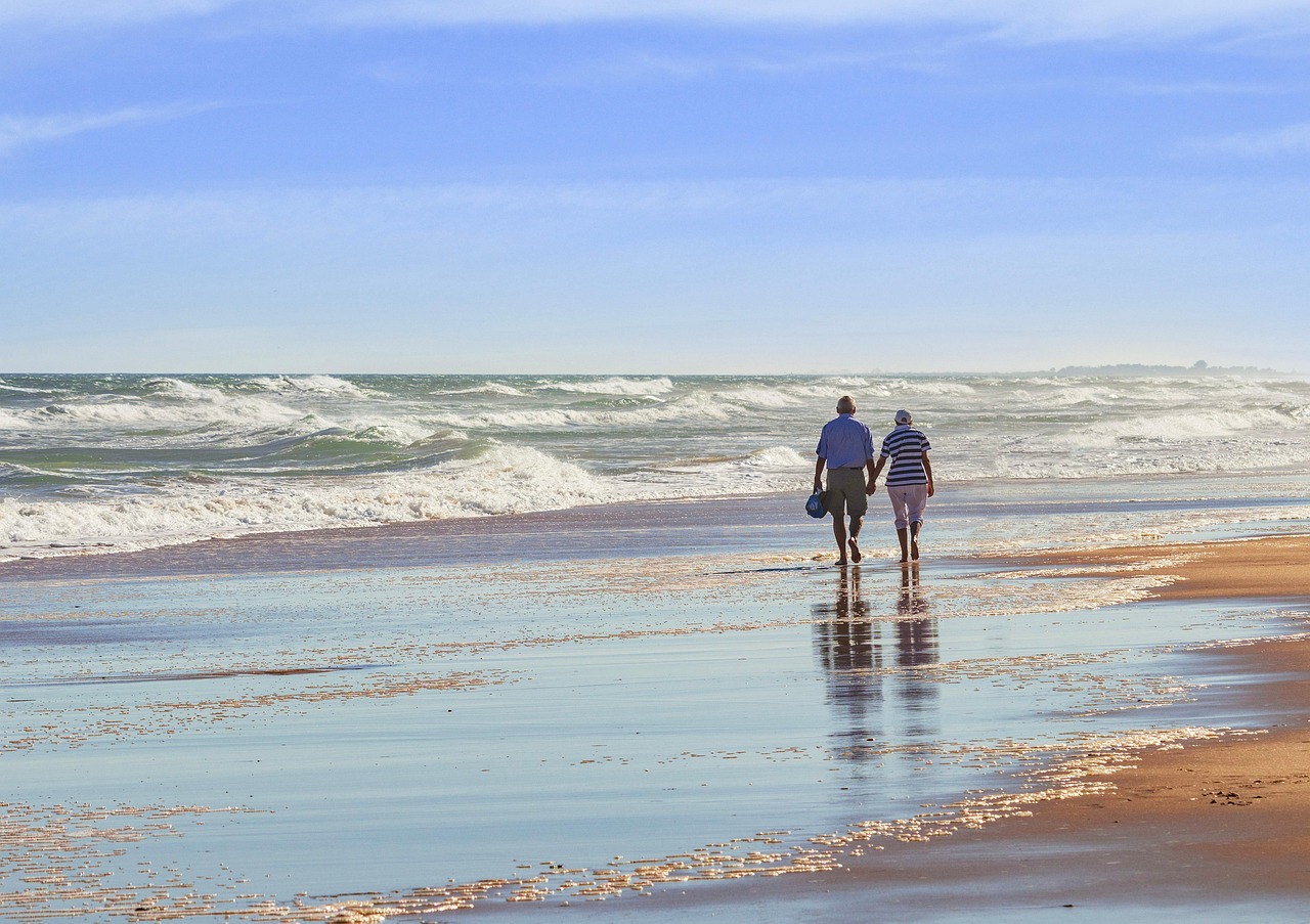 An older couple walking hand in hand along the shoreline at low tide